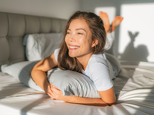 Woman laying in her bed smiling at the view outside.